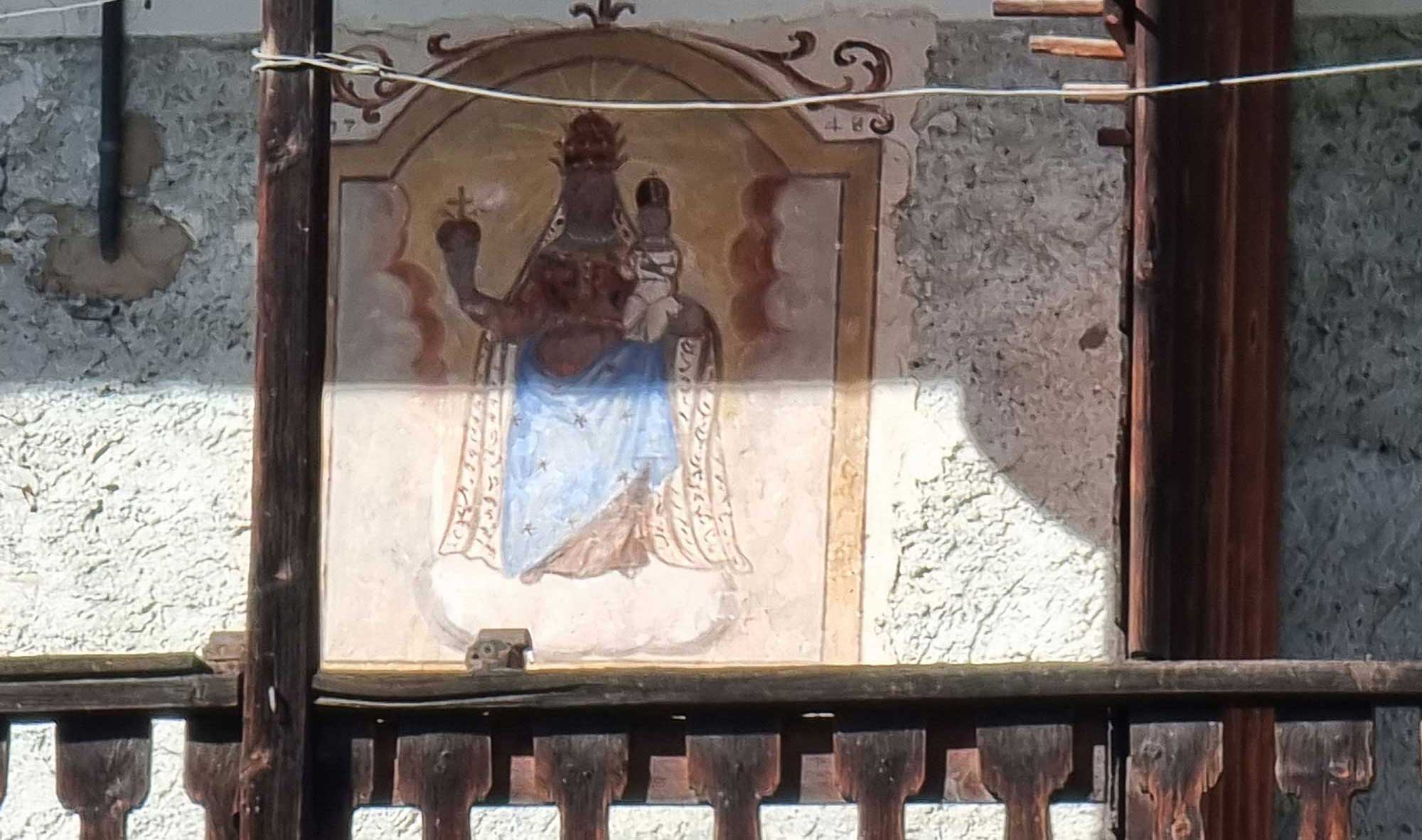 L’immagine rappresenta la Madonna d’Oropa nella sua iconografia classica: la Vergine nera, tra nubi, vestita di porpora e ammantata di azzurro sorregge il Bambino sul braccio sinistro. Madonna e Bambino sono coronati con la tiara. Quest’ultimo tiene nella mano sinistra un uccellino bianco, simbolo della passione. La Vergine regge con la destra un pomo rosso sormontato da una croce. Madre e Figlio portano una collana di perle al collo. Esterni alla cornice sono dipinti alcuni fregi.